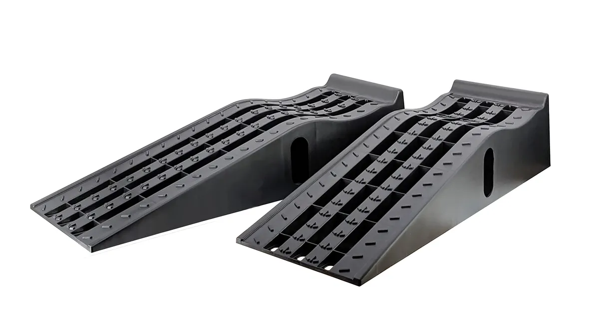 Pair of black molded plastic car service ramps with grooved tire channels on a garage floor