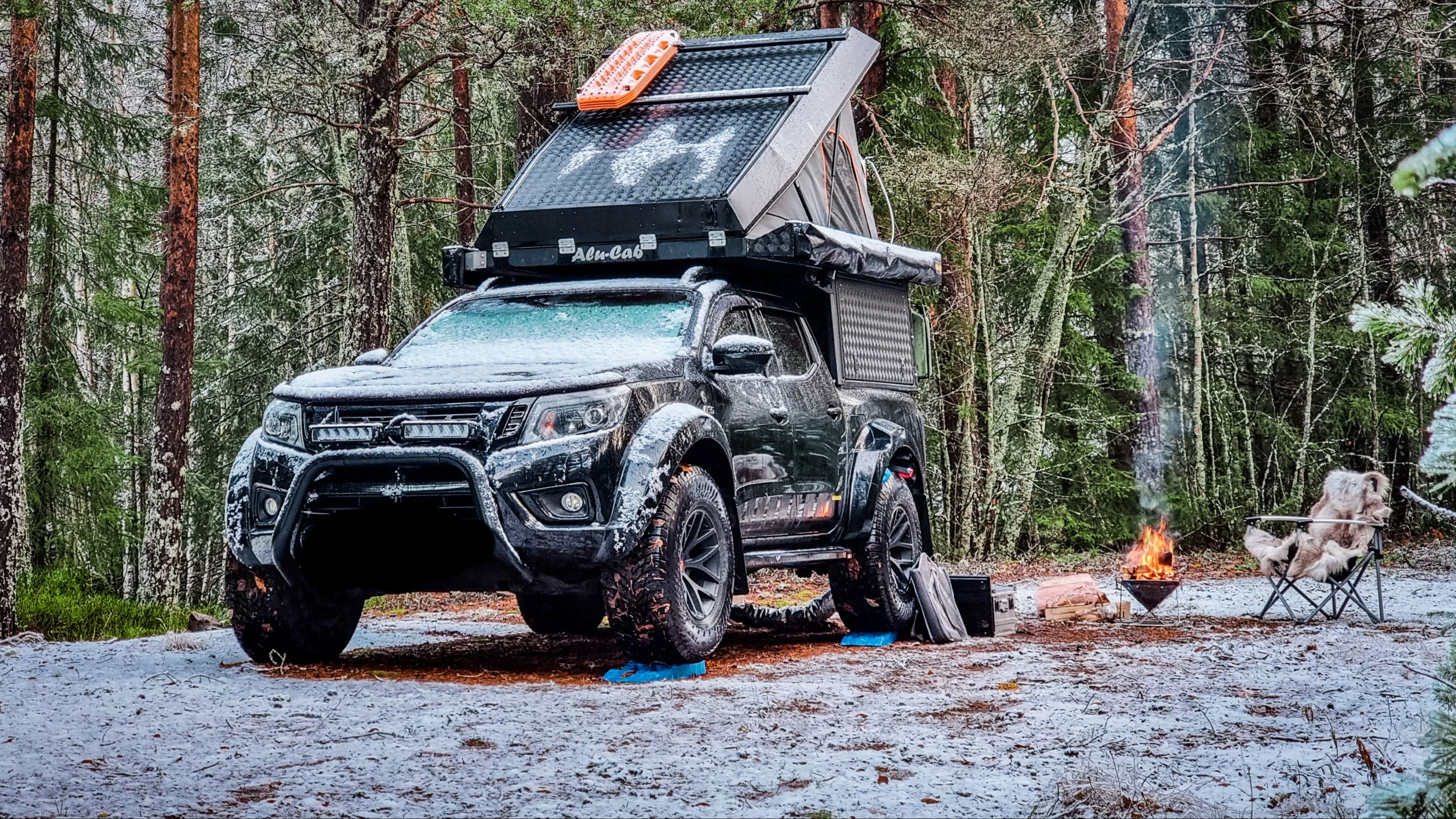 A pickup truck kitted with a rooftop tent, light bar and canopy camping in a snowy forest